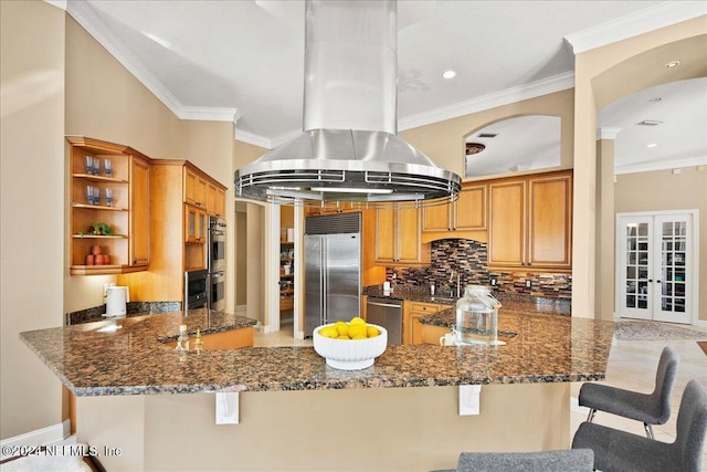 kitchen with french doors, dark stone counters, a kitchen bar, island range hood, and appliances with stainless steel finishes