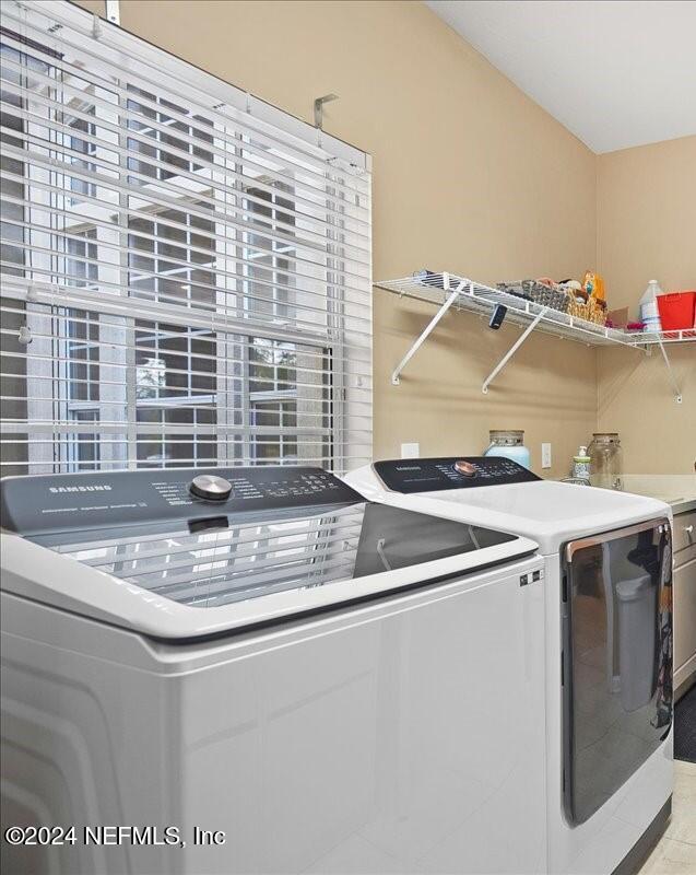 clothes washing area featuring separate washer and dryer, light tile patterned floors, and cabinets