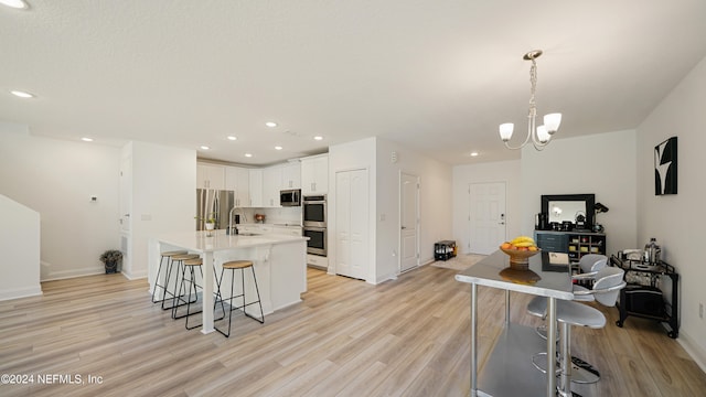 kitchen with an inviting chandelier, hanging light fixtures, white cabinetry, light wood-type flooring, and appliances with stainless steel finishes