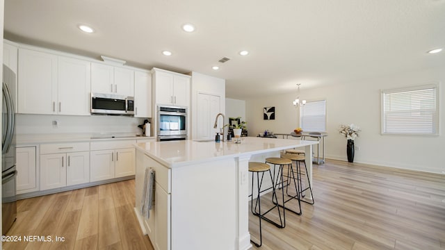 kitchen featuring white cabinets, appliances with stainless steel finishes, an island with sink, and light hardwood / wood-style flooring