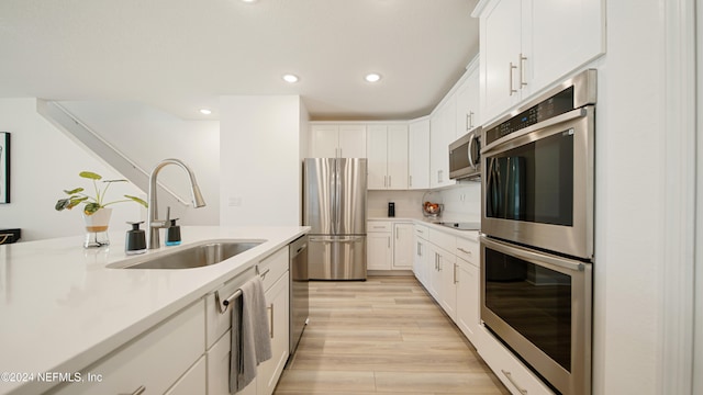 kitchen with white cabinetry, appliances with stainless steel finishes, backsplash, sink, and light hardwood / wood-style floors