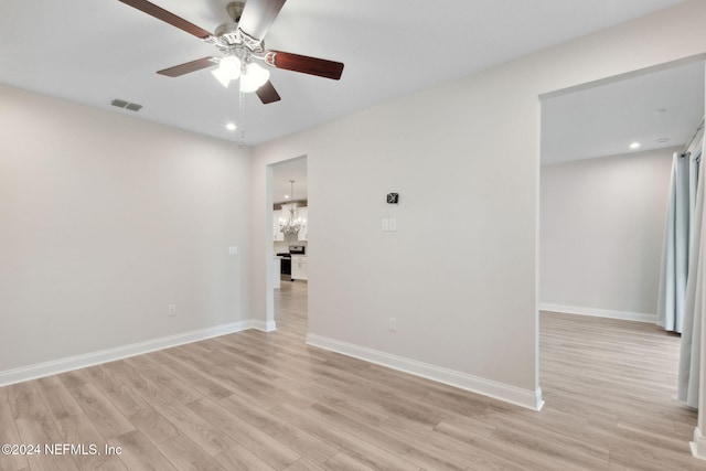 empty room featuring ceiling fan with notable chandelier and light hardwood / wood-style floors