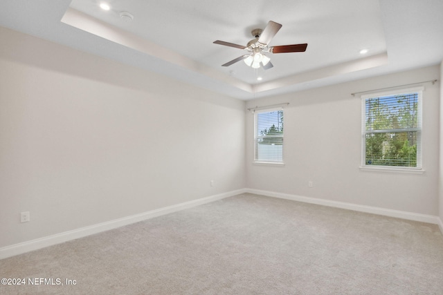 carpeted spare room with ceiling fan and a tray ceiling