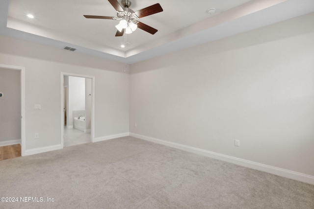 unfurnished bedroom featuring ceiling fan, light colored carpet, connected bathroom, and a tray ceiling