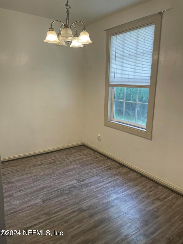 unfurnished room featuring an inviting chandelier and dark wood-type flooring