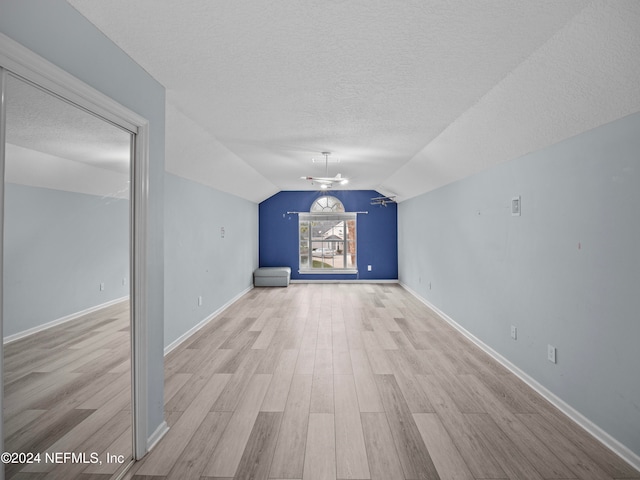 unfurnished living room with light hardwood / wood-style floors, a textured ceiling, and vaulted ceiling