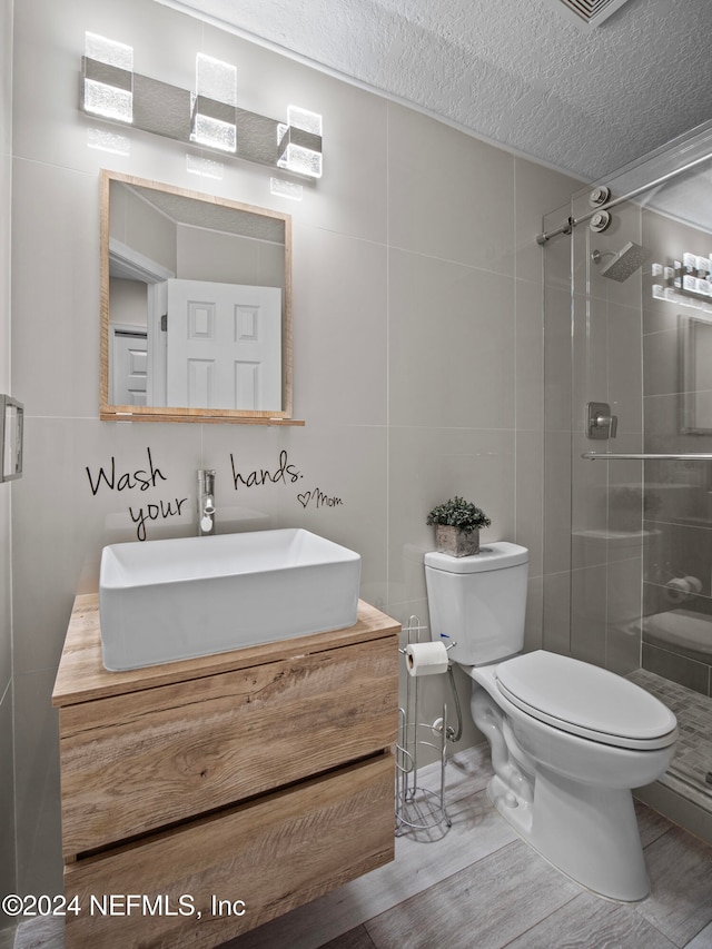 bathroom with a shower with door, wood-type flooring, a textured ceiling, toilet, and vanity