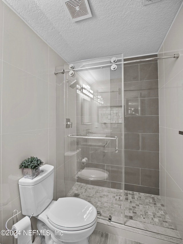 bathroom with toilet, a textured ceiling, and a shower with shower door