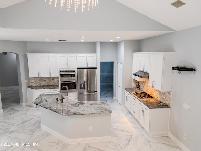 kitchen with decorative backsplash, a center island with sink, appliances with stainless steel finishes, white cabinetry, and light stone countertops