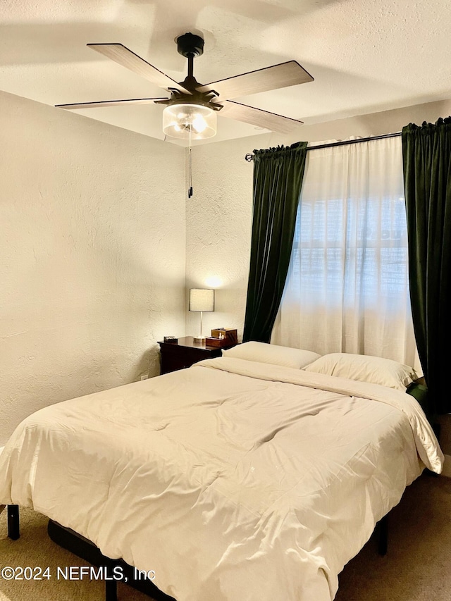 carpeted bedroom featuring ceiling fan and a textured ceiling