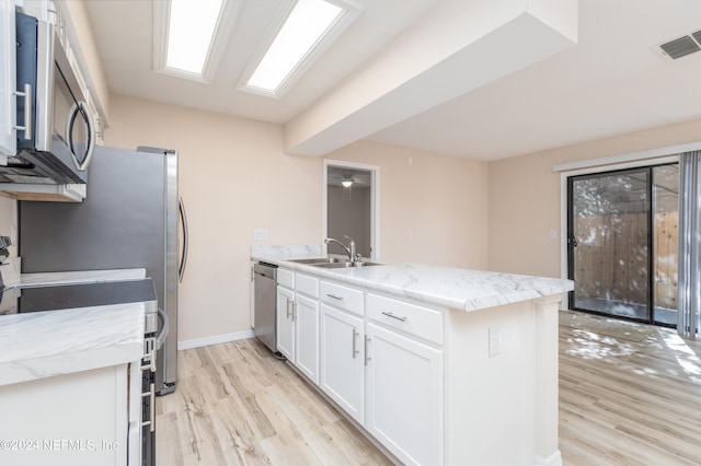 kitchen with stainless steel appliances, light stone countertops, sink, white cabinets, and light hardwood / wood-style flooring