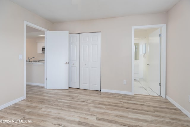 unfurnished bedroom with light hardwood / wood-style floors, connected bathroom, a closet, and sink