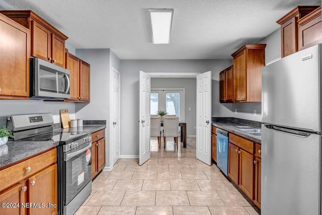 kitchen featuring appliances with stainless steel finishes, dark stone countertops, a textured ceiling, and light tile patterned floors