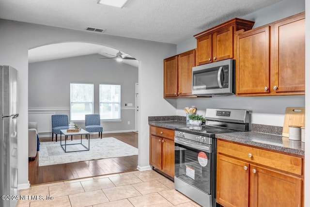 kitchen featuring light wood-type flooring, a textured ceiling, ceiling fan, stainless steel appliances, and vaulted ceiling