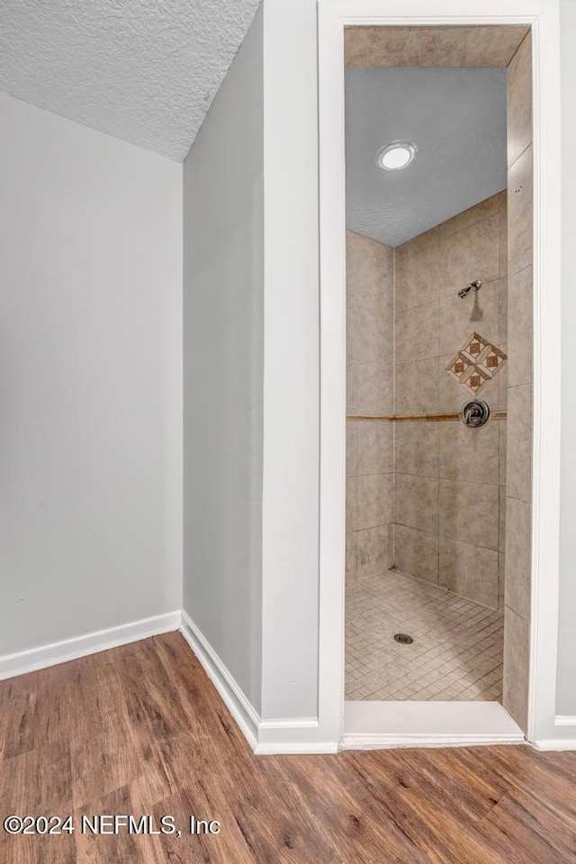 bathroom featuring a textured ceiling, wood-type flooring, and tiled shower