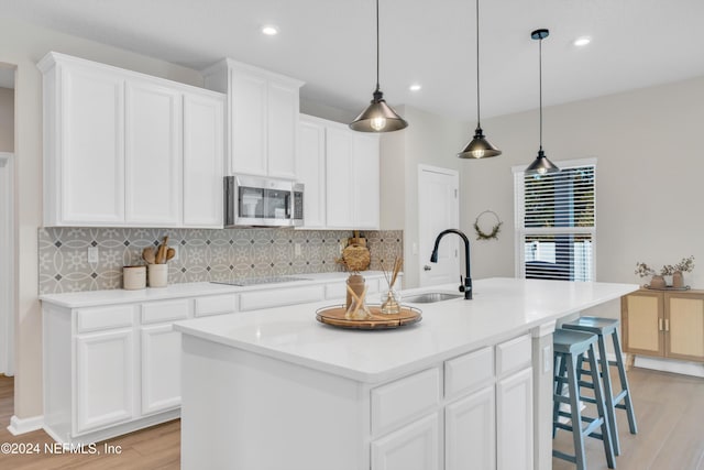 kitchen with a center island with sink, white cabinets, light wood-type flooring, and sink