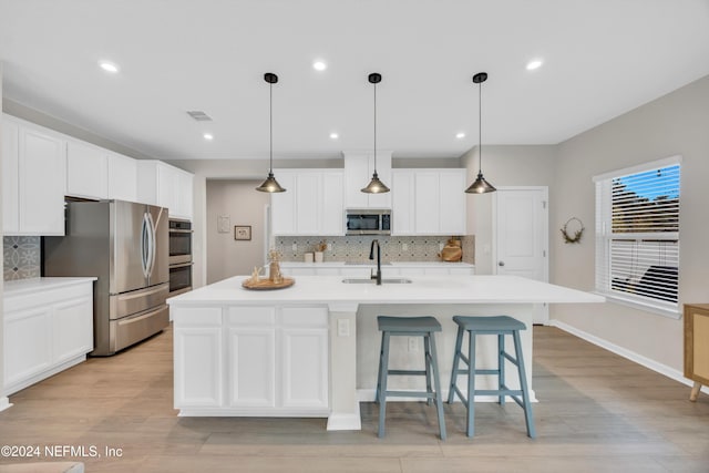 kitchen featuring sink, an island with sink, decorative backsplash, appliances with stainless steel finishes, and light wood-type flooring