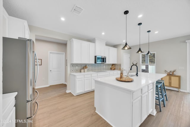 kitchen featuring a kitchen island with sink, white cabinets, light hardwood / wood-style flooring, decorative light fixtures, and stainless steel appliances