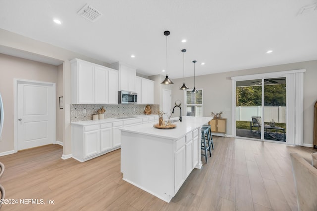 kitchen with backsplash, pendant lighting, light hardwood / wood-style floors, a kitchen island with sink, and white cabinets