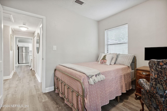 bedroom featuring wood-type flooring, stainless steel fridge, and a textured ceiling