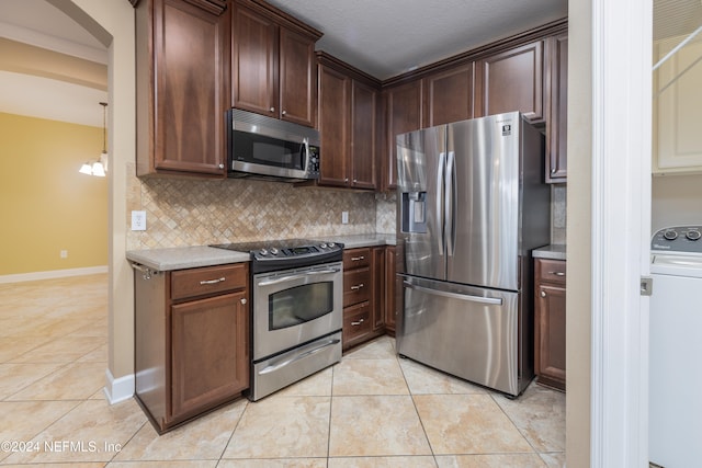 kitchen featuring washer / clothes dryer, a chandelier, appliances with stainless steel finishes, light tile patterned floors, and backsplash