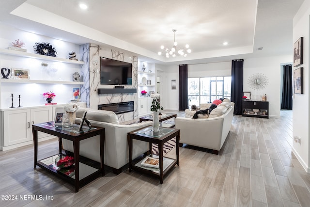 living room featuring light hardwood / wood-style floors, a tray ceiling, built in features, a fireplace, and a chandelier