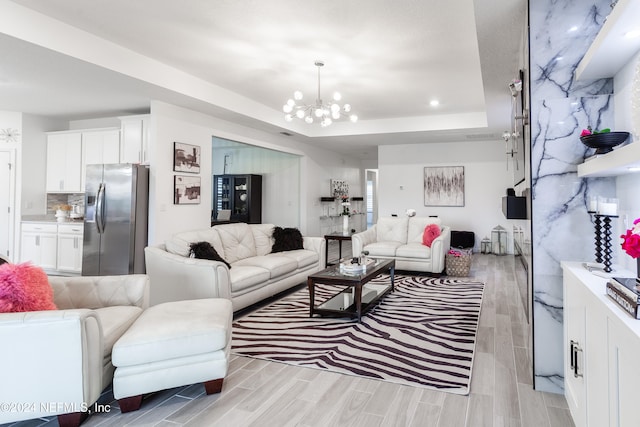 living room with a notable chandelier, a raised ceiling, and light wood-type flooring