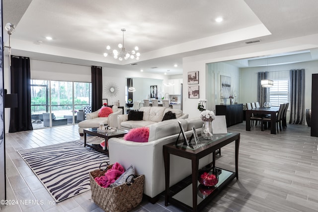 living room featuring a healthy amount of sunlight, a raised ceiling, light hardwood / wood-style flooring, and an inviting chandelier