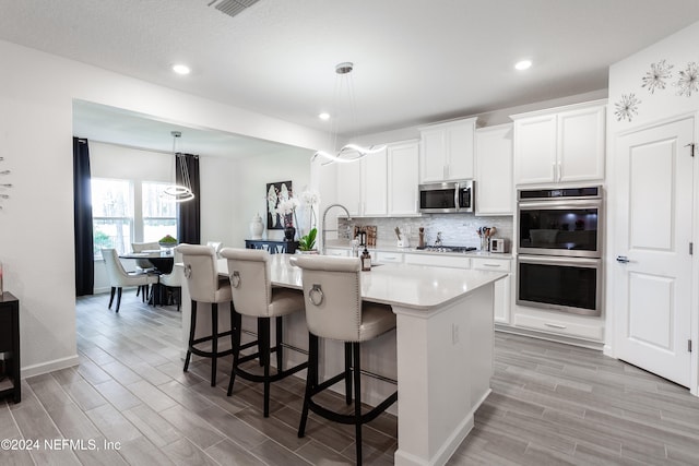 kitchen featuring a kitchen island with sink, a kitchen breakfast bar, appliances with stainless steel finishes, decorative light fixtures, and white cabinetry