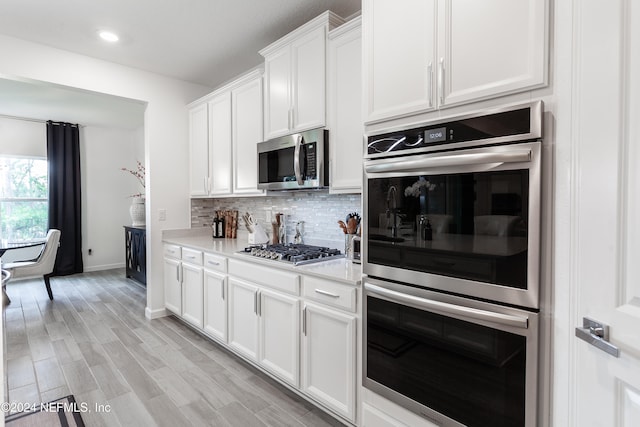 kitchen featuring decorative backsplash, light hardwood / wood-style floors, light stone counters, white cabinetry, and stainless steel appliances