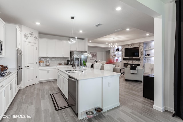 kitchen featuring pendant lighting, a kitchen island with sink, white cabinetry, stainless steel appliances, and a chandelier