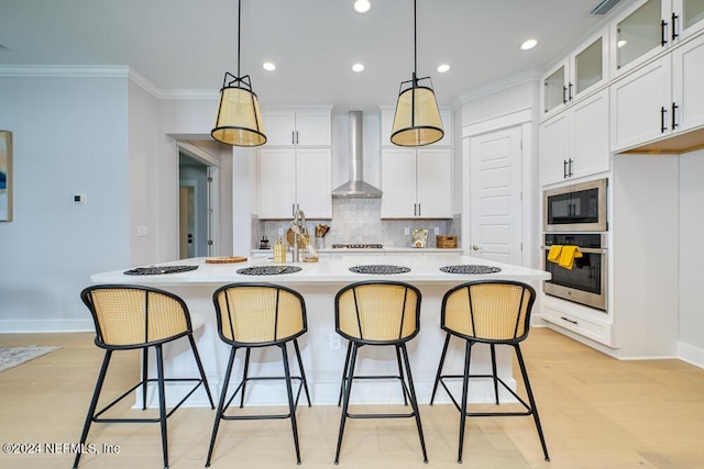 kitchen with wall chimney exhaust hood, built in microwave, a center island with sink, white cabinets, and oven