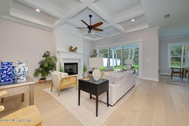 living room with ceiling fan, a large fireplace, coffered ceiling, light wood-type flooring, and ornamental molding