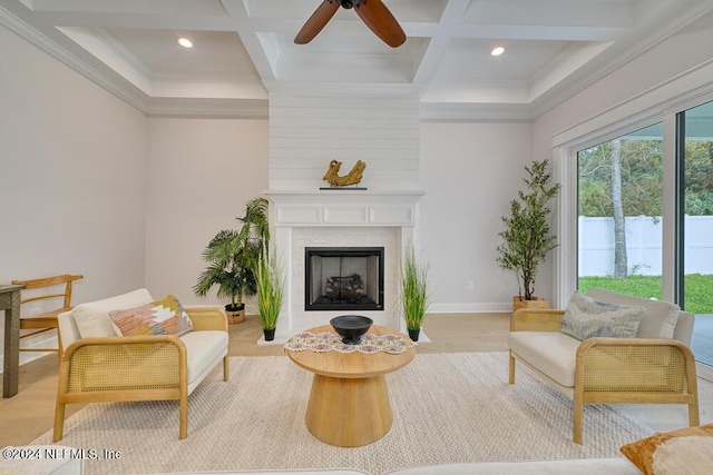 sitting room with light wood-type flooring, ornamental molding, coffered ceiling, a large fireplace, and beamed ceiling