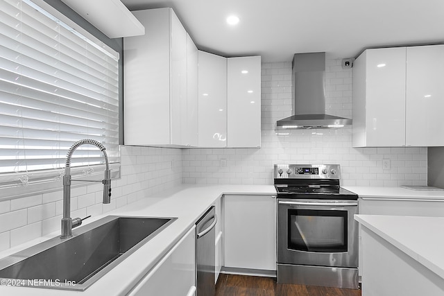 kitchen featuring stainless steel appliances, wall chimney exhaust hood, white cabinets, and sink