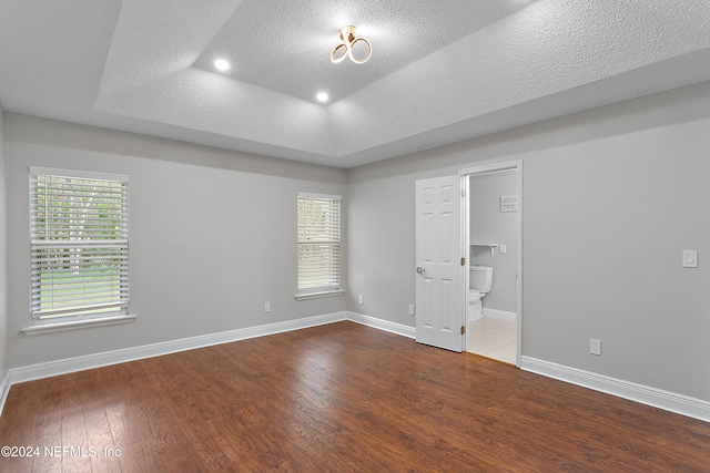 unfurnished bedroom with connected bathroom, hardwood / wood-style floors, a raised ceiling, and a textured ceiling