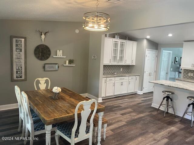 dining area with dark wood-type flooring, vaulted ceiling, and an inviting chandelier