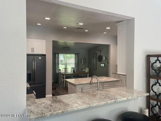 kitchen featuring kitchen peninsula, black refrigerator with ice dispenser, a kitchen bar, white cabinetry, and light stone counters