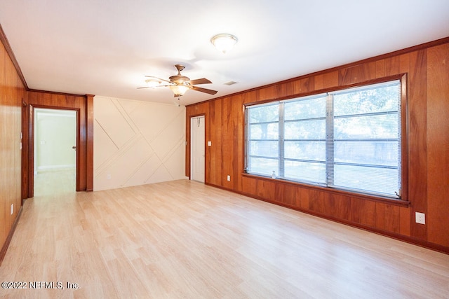 empty room featuring wood walls, ceiling fan, and light hardwood / wood-style flooring