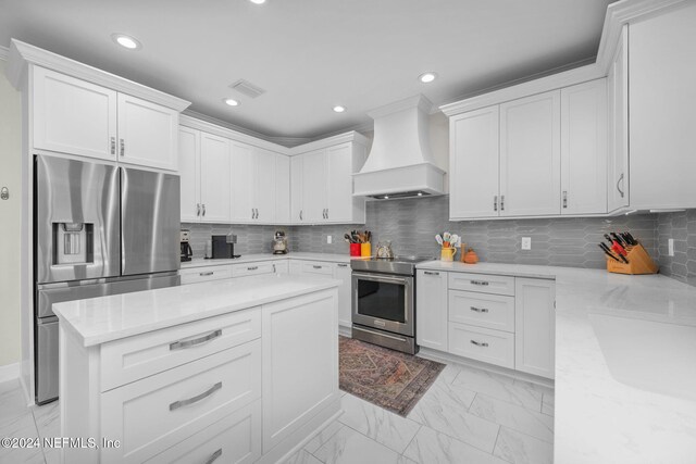 kitchen featuring tasteful backsplash, white cabinetry, custom range hood, and stainless steel appliances