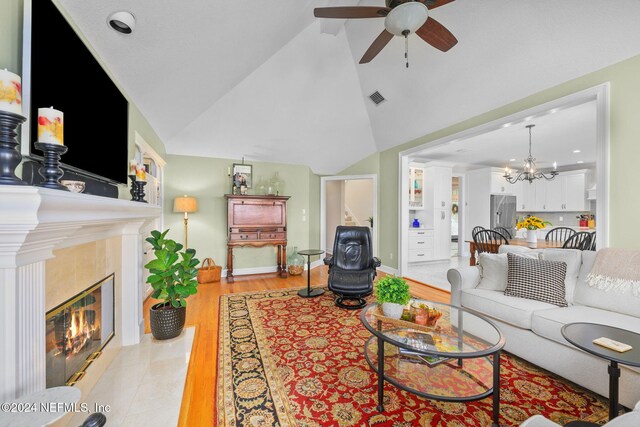 living room featuring a tiled fireplace, ceiling fan with notable chandelier, light hardwood / wood-style flooring, and lofted ceiling