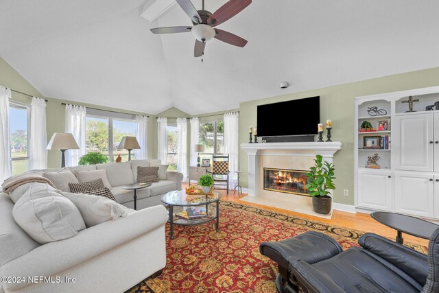 living room featuring ceiling fan, hardwood / wood-style flooring, vaulted ceiling with beams, and a fireplace