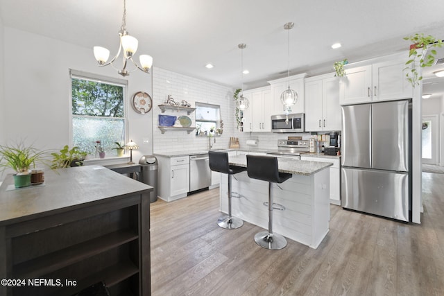 kitchen with white cabinetry, light hardwood / wood-style flooring, hanging light fixtures, and appliances with stainless steel finishes