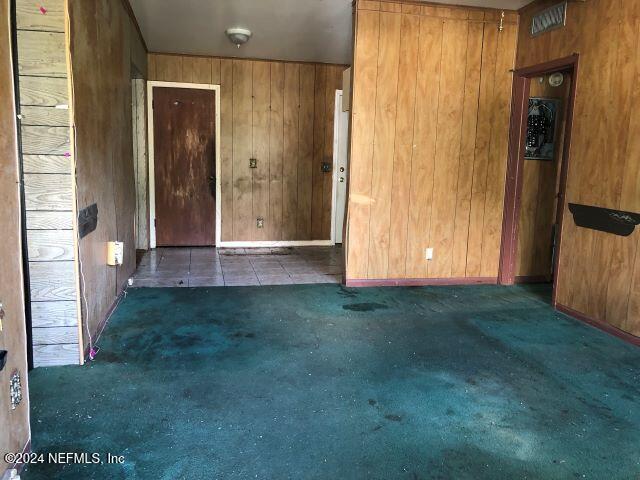 carpeted empty room featuring wood walls