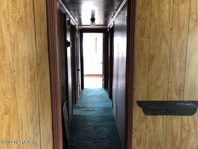 hallway with wood walls and dark colored carpet