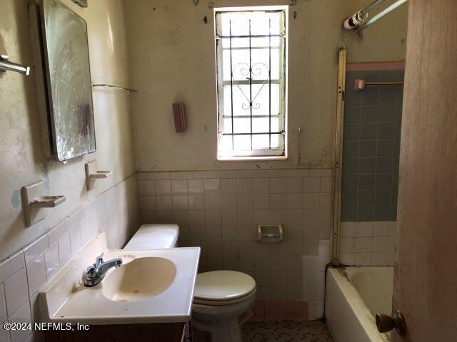 full bathroom featuring tile walls, vanity, tiled shower / bath, and toilet