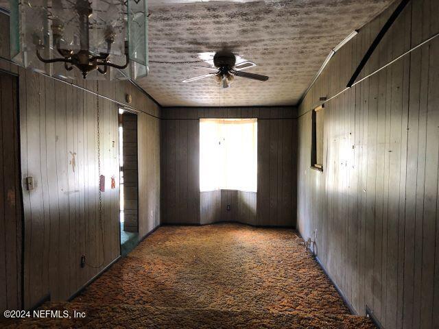 empty room with wooden walls, carpet flooring, and ceiling fan with notable chandelier