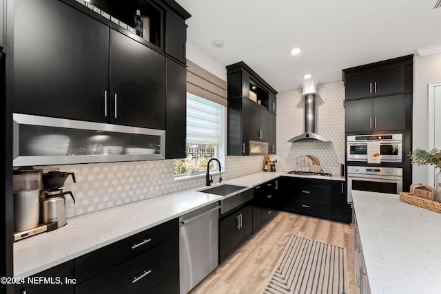 kitchen with light hardwood / wood-style floors, wall chimney exhaust hood, sink, backsplash, and appliances with stainless steel finishes