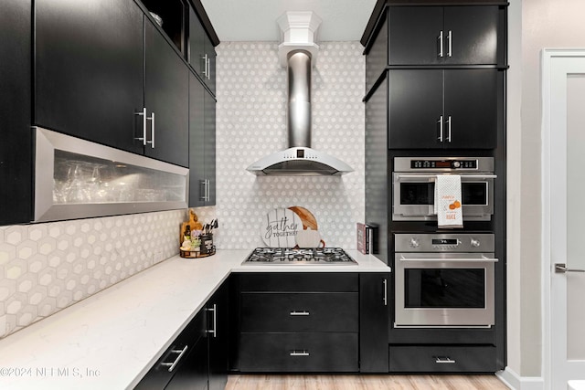 kitchen with light hardwood / wood-style flooring, decorative columns, wall chimney exhaust hood, and stainless steel appliances