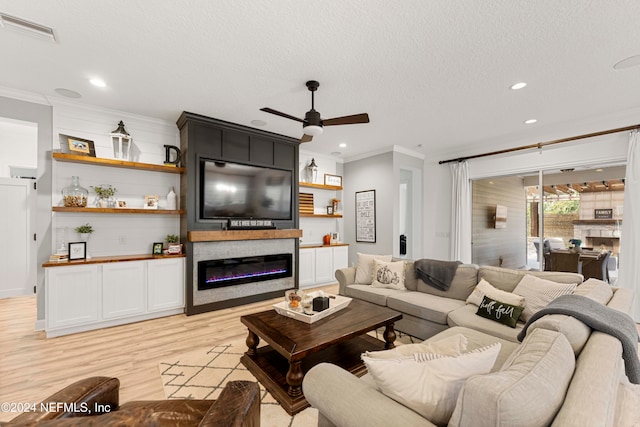 living room featuring a textured ceiling, ceiling fan, crown molding, light wood-type flooring, and a large fireplace